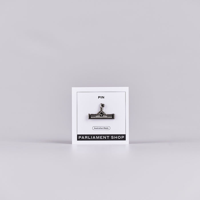 Silver and grey coloured pin in the shape of Australian Parliament House on a white backing card.