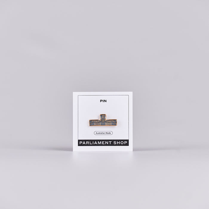 Gold and grey coloured pin in the shape of Australian Parliament House on a white backing card.