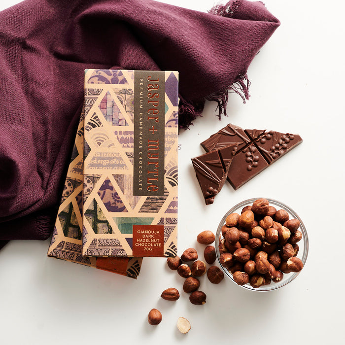 Brown chocolate box with a purple pattern with hazelnuts and chocolate block on a table.