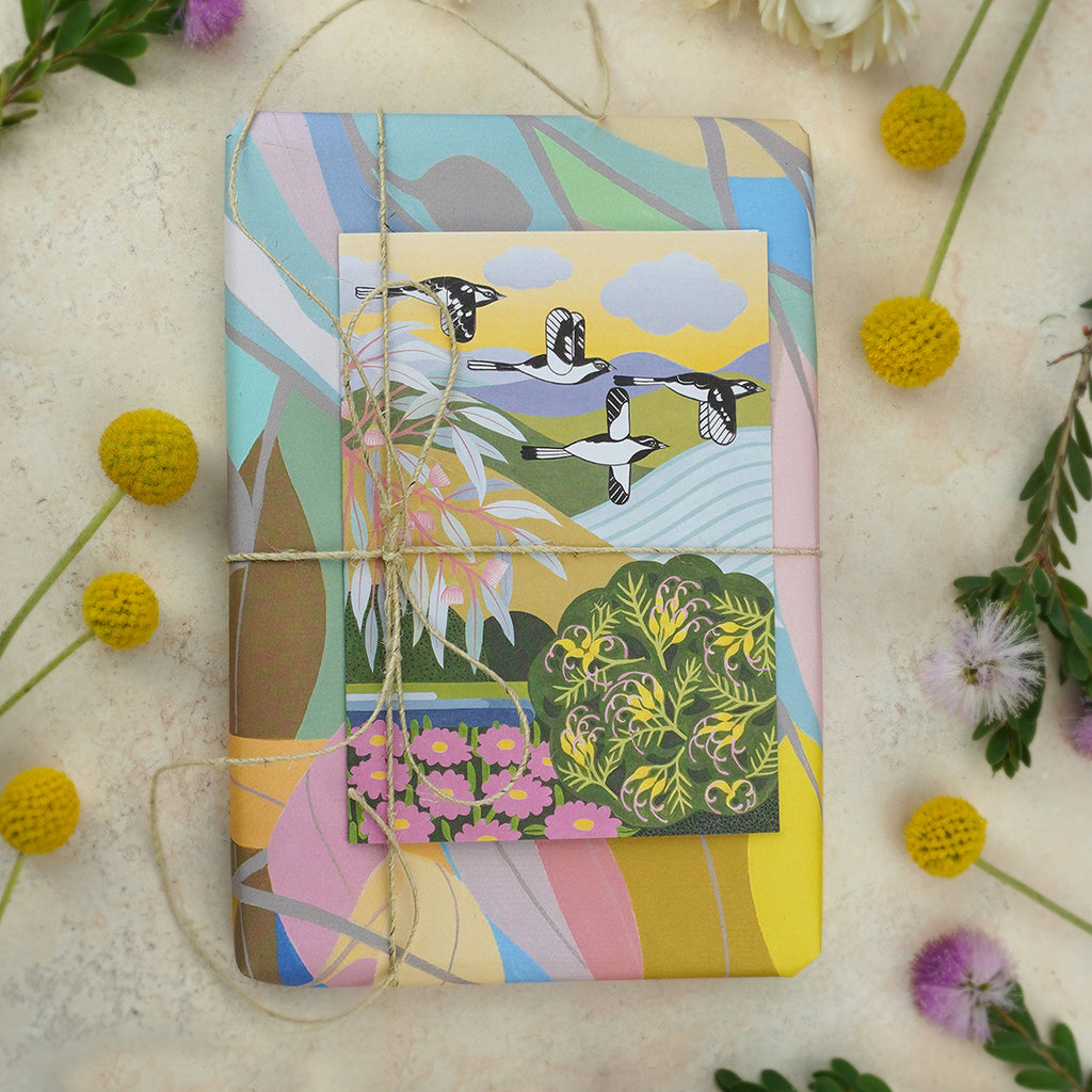 Flat lay of a wrapped present with a colourful leaf print and a greeting card on top with birds and trees.