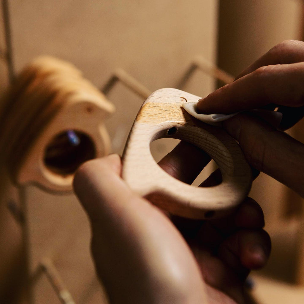 Hands wiping a wooden baby bird rattle with a cloth.