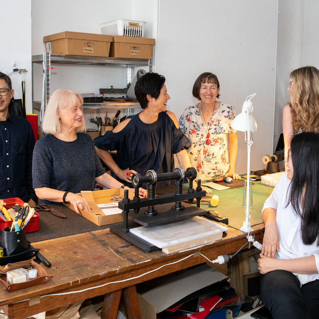 Six people sitting around a table in a studio workshop smiling.