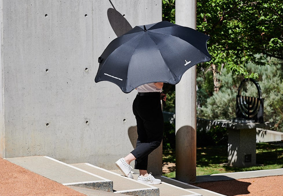 Woman with large open golf umbrella with Parliament House building logo on it.