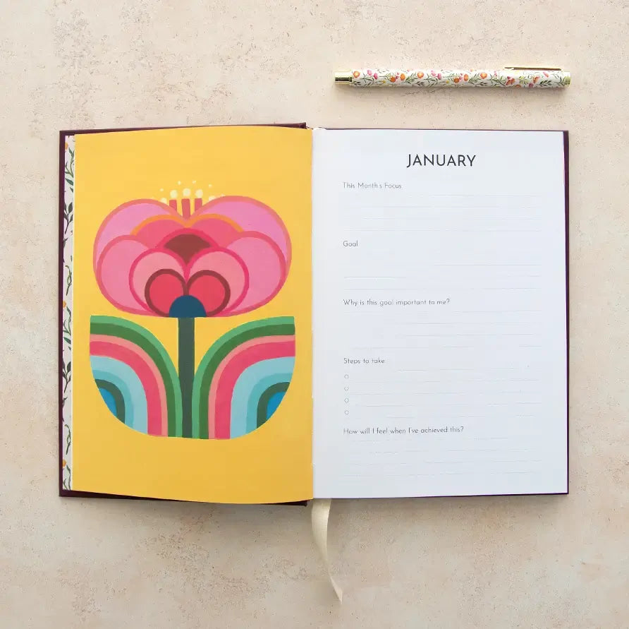 Open notebook with a colorful floral design on a yellow page and a pen on a beige surface.