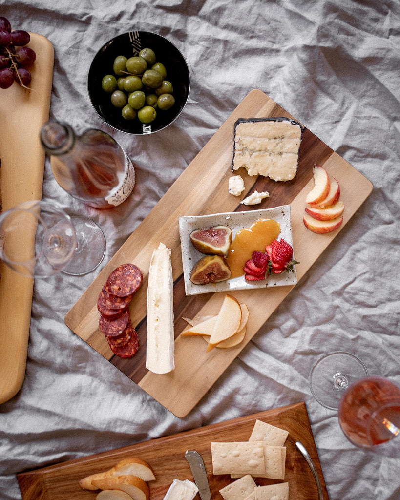 wooden serving board surrounded by an assortment of cheese, charcuterie and wine