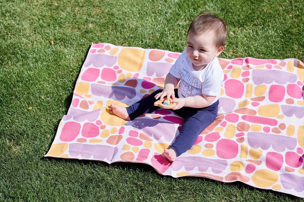 toddler sitting on top of pink blanket holding wooden rattle