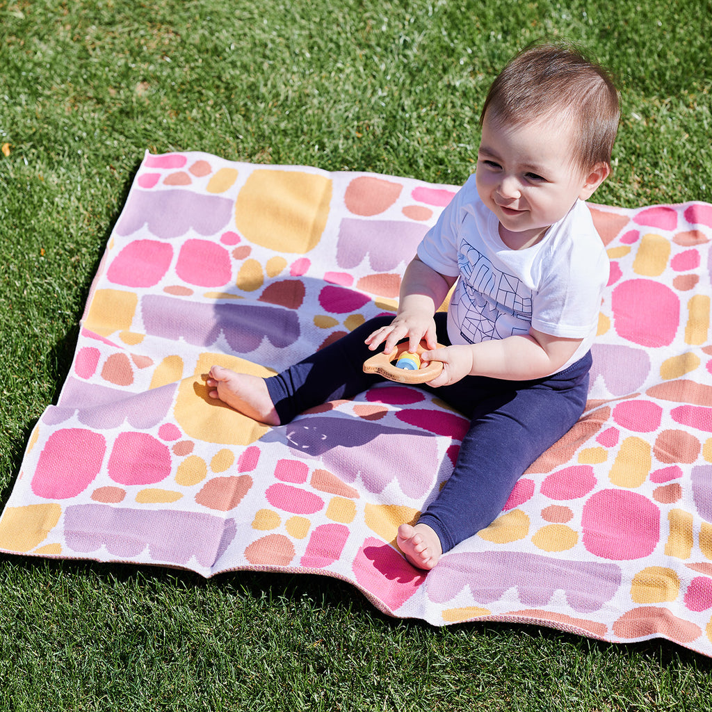 toddler sitting on top of pink blanket holding wooden rattle