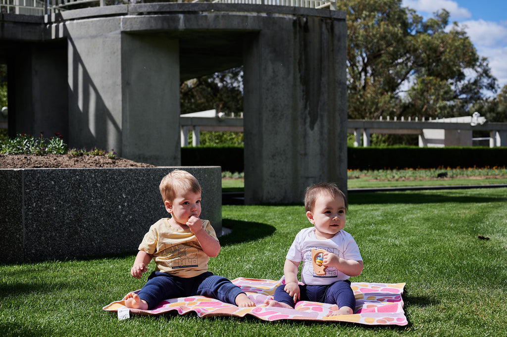 two toddlers sitting on top of a pink blanket 