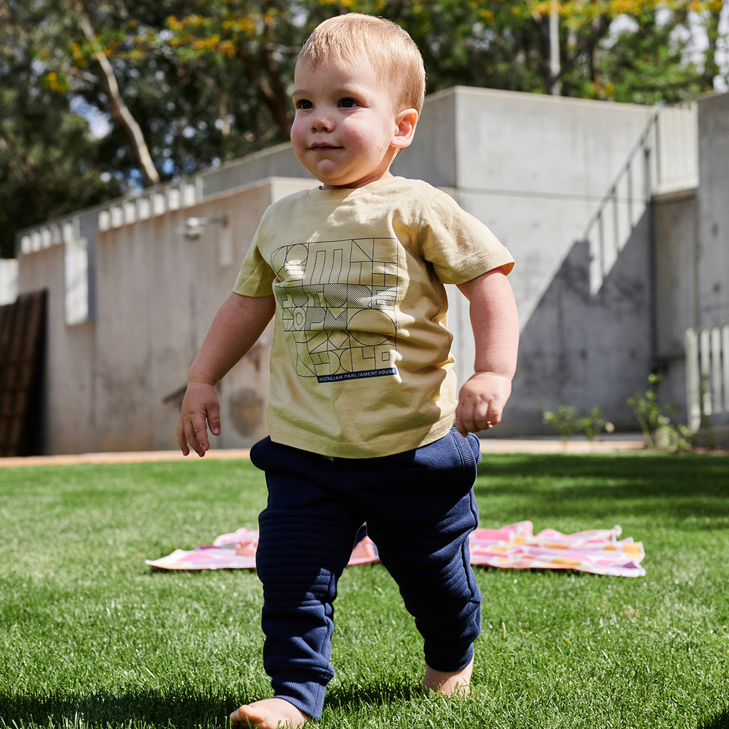 toddler walking on grass wearing mustard yellow t-shirt and navy pants