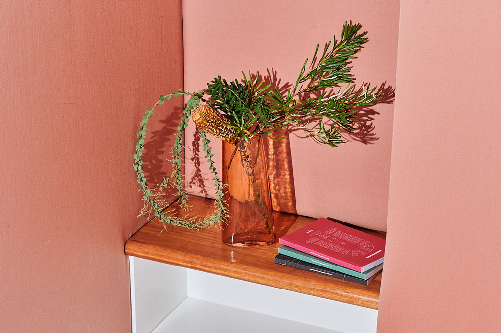 Glass Vase with green plants, placed next to a stack of notebooks