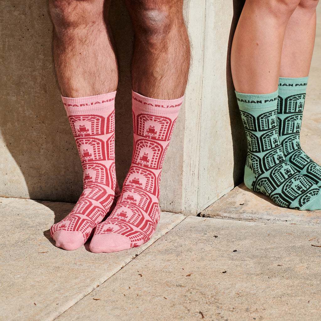 two pairs of feet standing against different sides of a wall. One is wearing pink socks and the other green socks