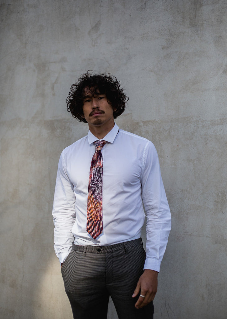 Man wearing a white shirt, black pants and navy blue tie with white and orange details