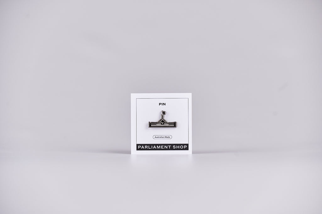 Silver and grey coloured pin in the shape of Australian Parliament House on a white backing card.