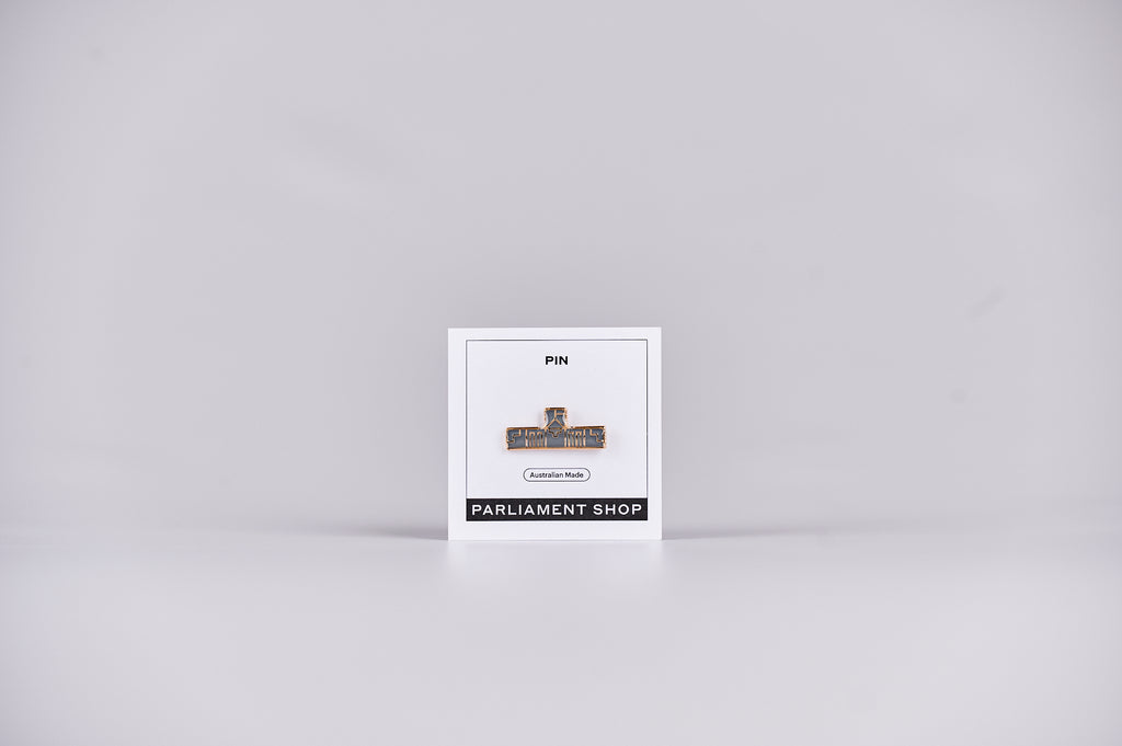 Gold and grey coloured pin in the shape of Australian Parliament House on a white backing card. 