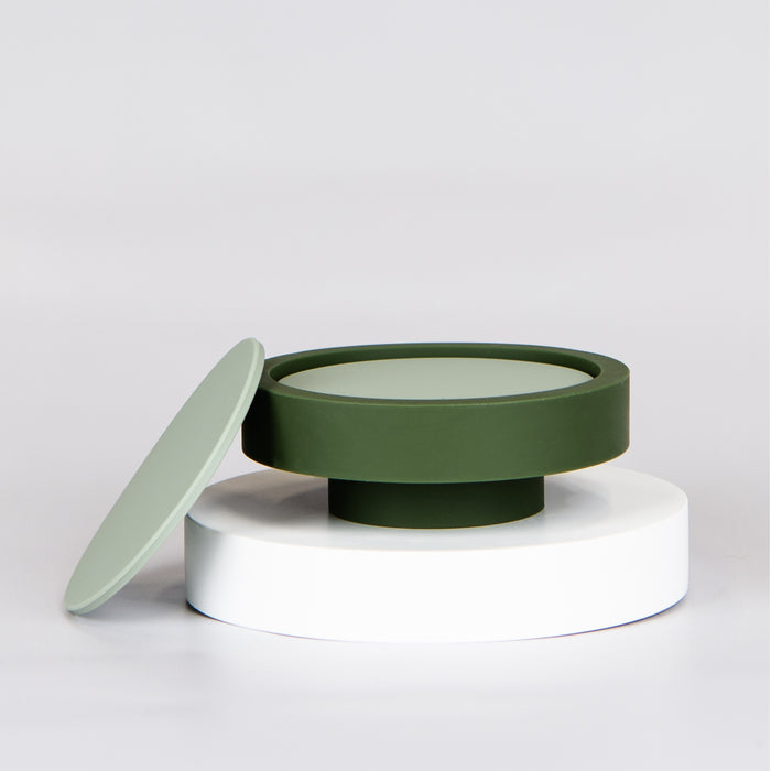 Round light green silicone coasters in a dark green base on top of a small round circle plinth with one coaster leaning against the side.