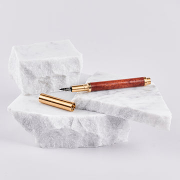 A fountain pen with a wood barrel and brass cap and trims arranged on pieces of marble.