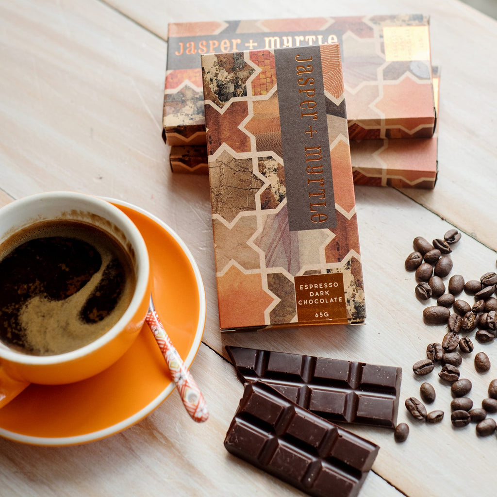 Chocolate box with a orange and brown pattern with a coffee, coffee beans and chocolate block on a table.