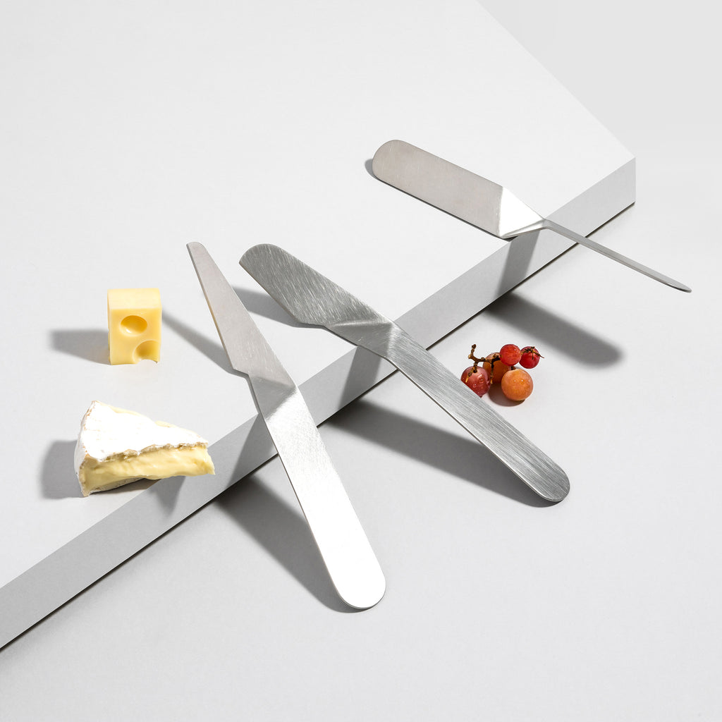 Set of 3 stainless steel cheese knives, surounded by cheese and grapes