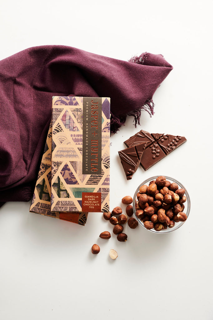 Brown chocolate box with a purple pattern with hazelnuts and chocolate block on a table.