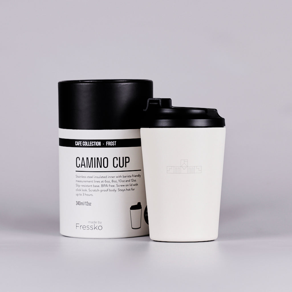 White reusable coffee cup with black geometric logo inspired by the Parliament House building, next to a white cylindrical box. 