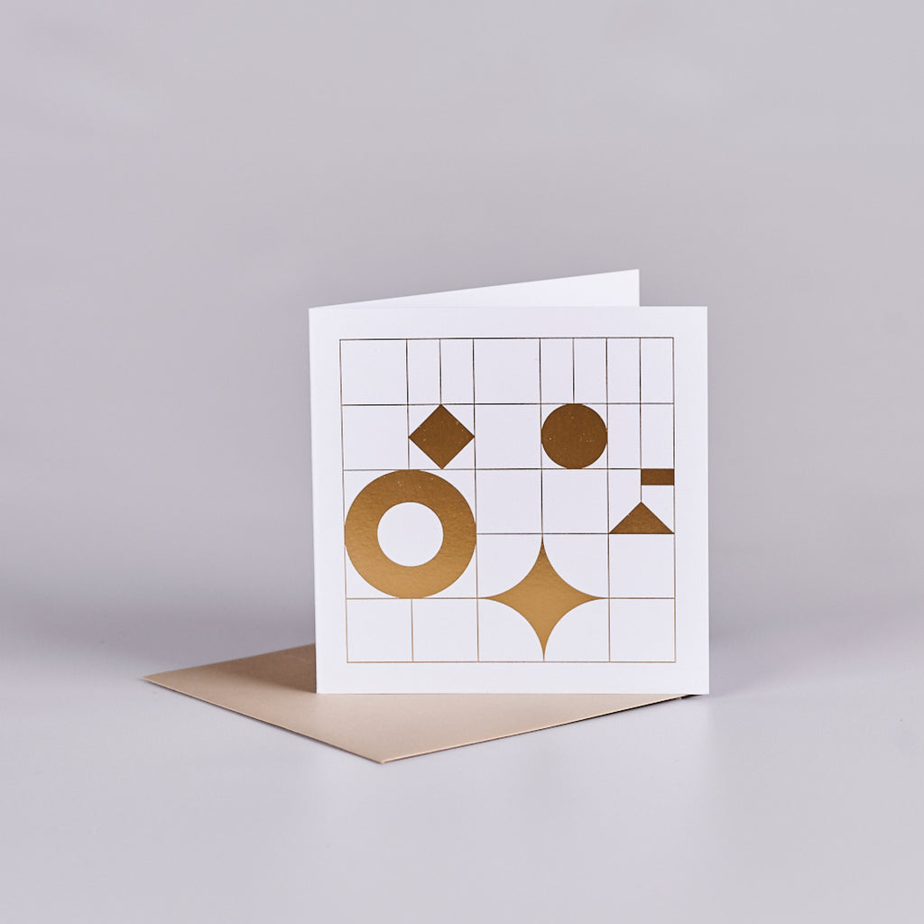 White card with a grid design and gold shapes. The card is sitting on a gold envelope.
