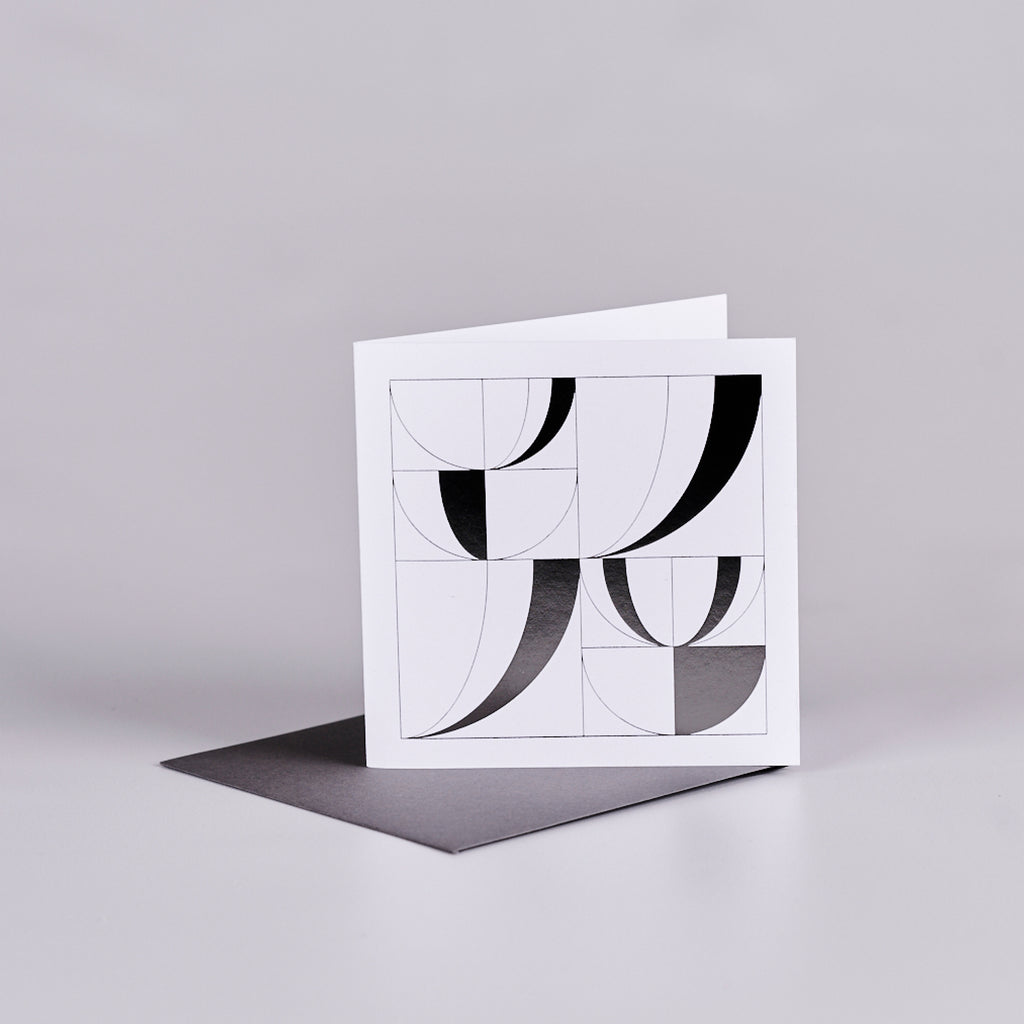 White square gift card with a black geometric design in the shape of open books. The card is sitting on top of a black envelope.