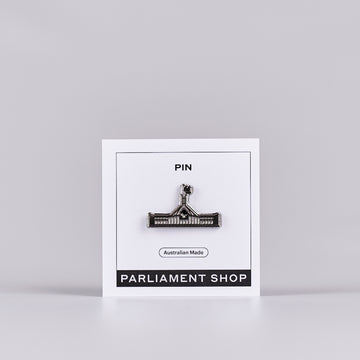 Silver and grey coloured pin in the shape of Australian Parliament House on a white backing card.