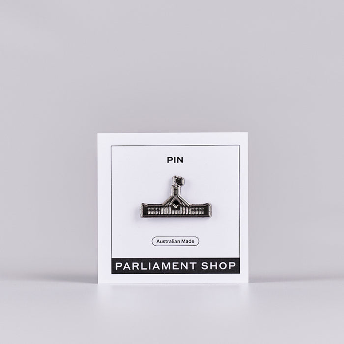 Silver and grey coloured pin in the shape of Australian Parliament House on a white backing card.
