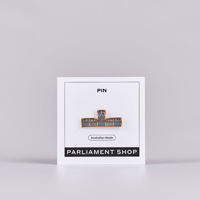 Gold and grey coloured pin in the shape of Australian Parliament House on a white backing card. 