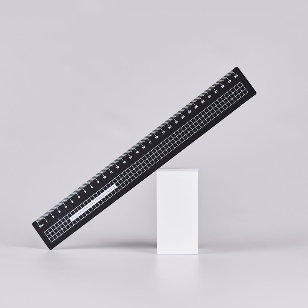 Black ruler with a white grid design and text reading 'Australian Parliament House'.