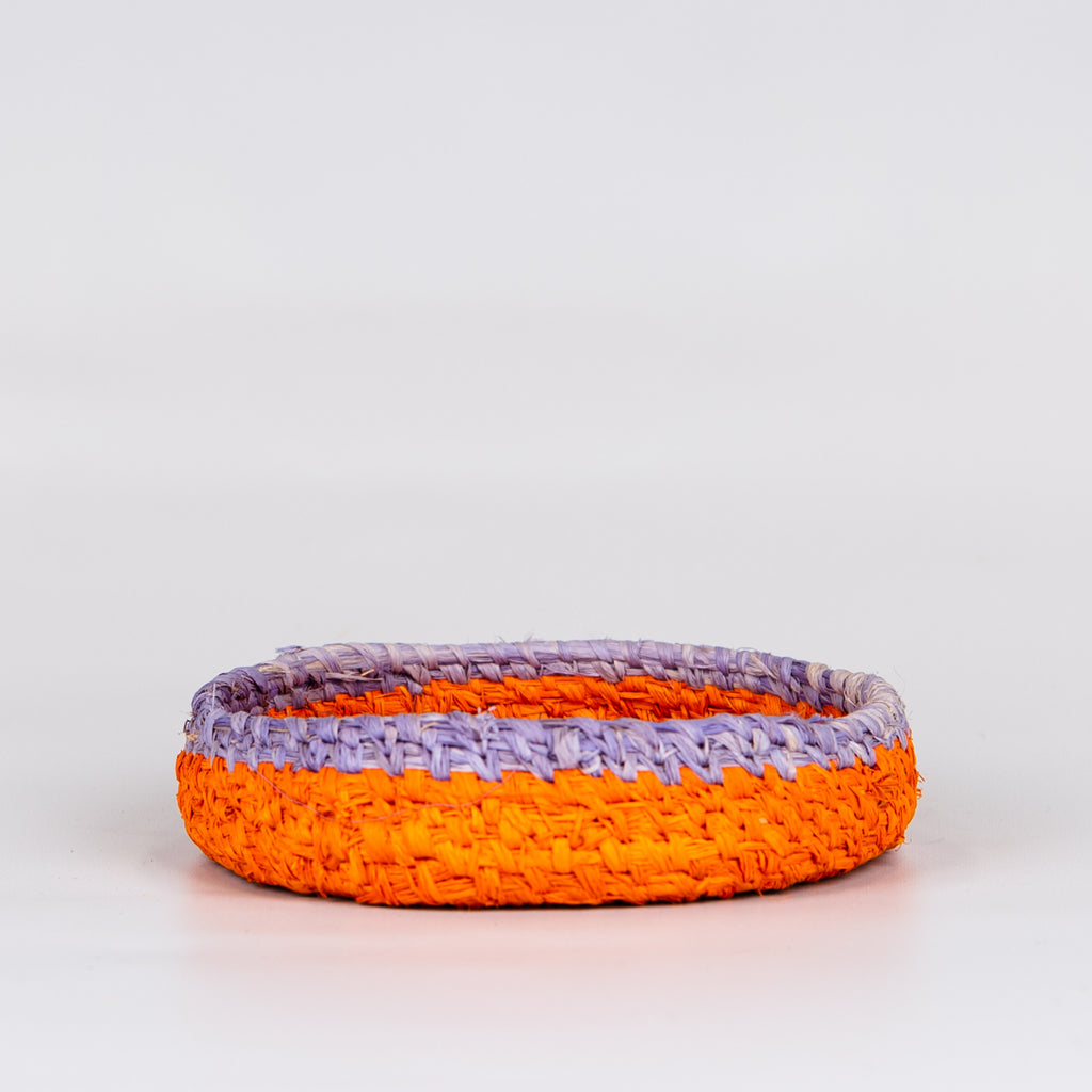Side of grass woven basket in orange and purple colours.