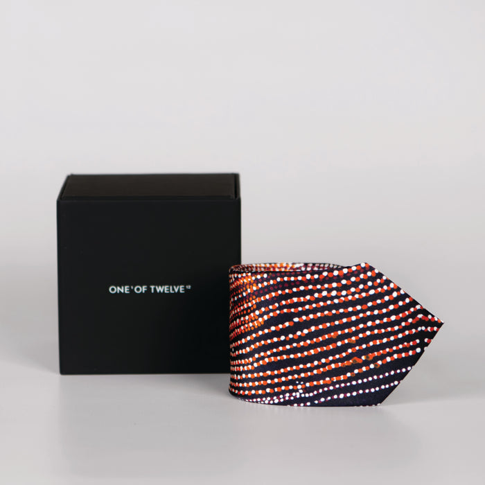 a rolled navy blue tie with white and orange details and black display box
