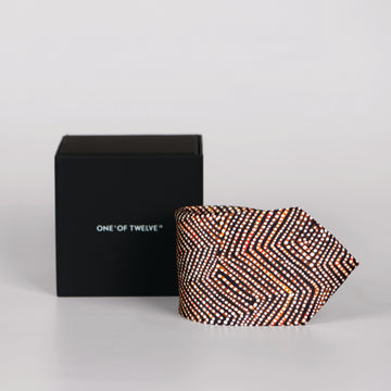 A rolled brown, white and black tie with dot and line detail and a black display box