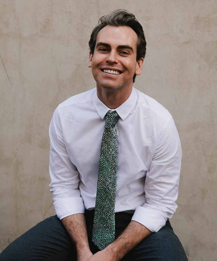 a man smiling wearing a white shirt, black pants and a dotted blue tie