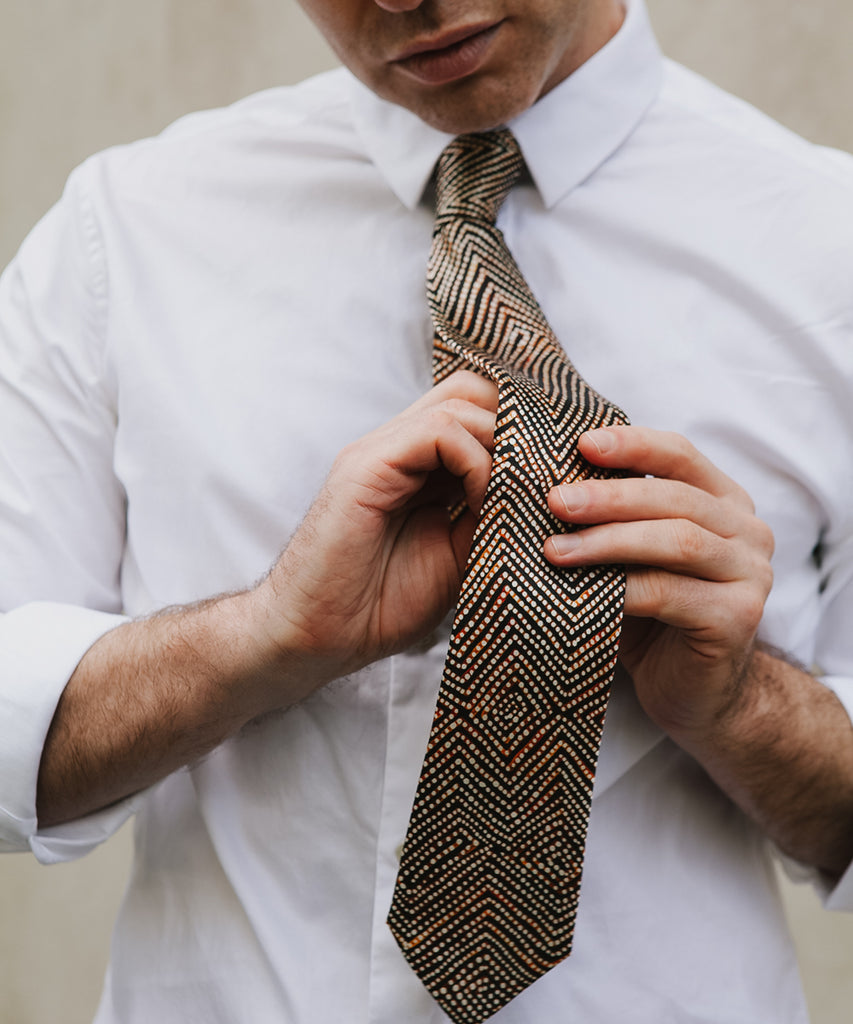 Man wearing a white shirt putting on a black, brown and white tie