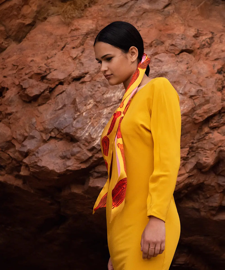 woman posing in front of red rock wearing a yellow dress and vibrant scarf tied to hair